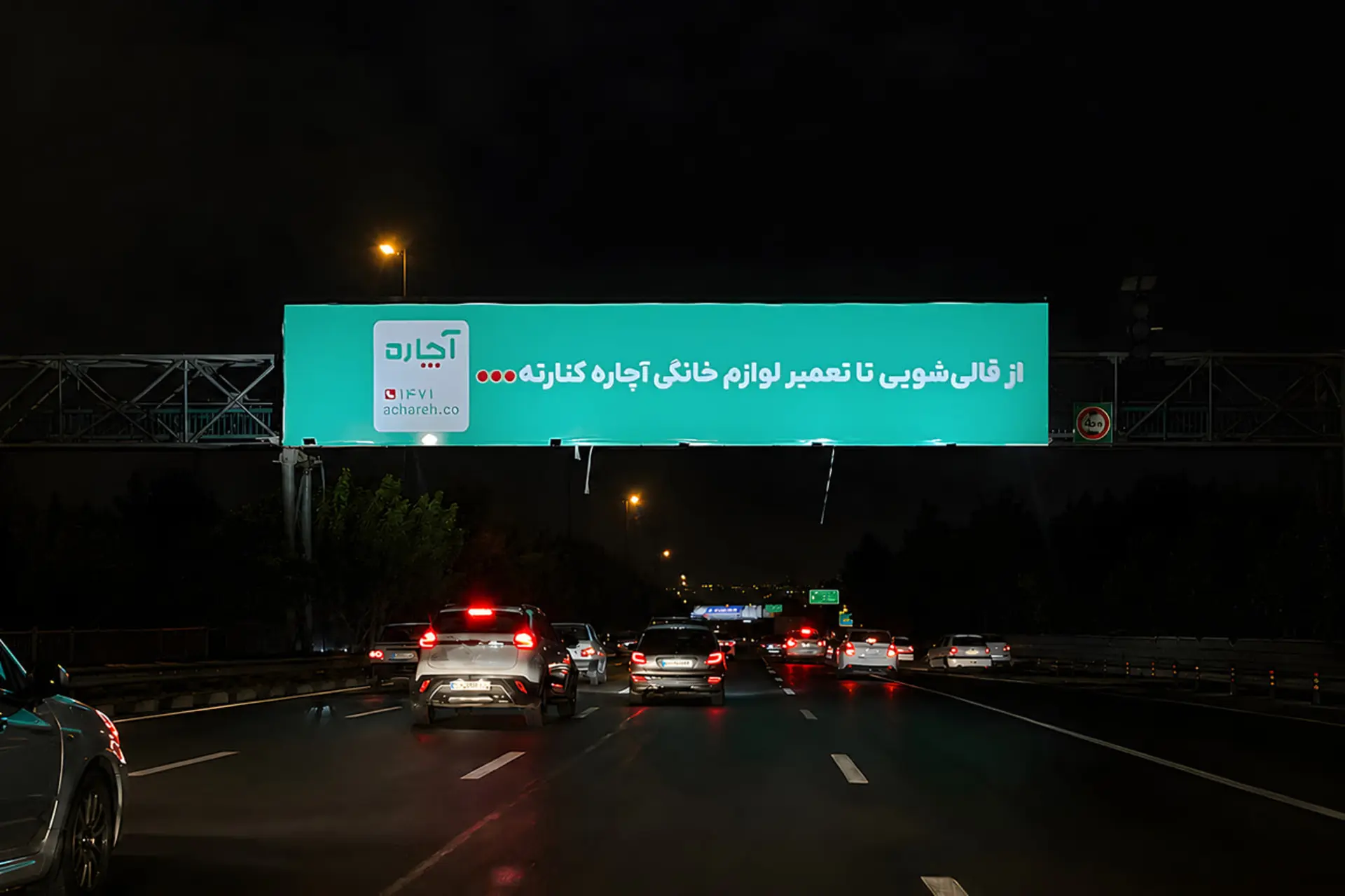 بیلبورد درخشان آچاره (Achareh) در شب بر فراز بزرگراه پرتردد