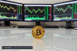 سکه طلایی بیت‌کوین (Bitcoin) روی میز در مقابل نمایشگرهای تحلیل بازار