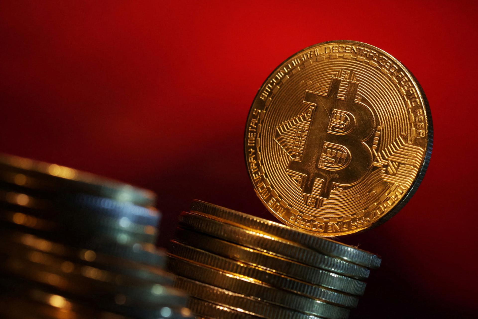 سکه طلایی بیت کوین (Bitcoin) روی دو دسته سکه در پس‌زمینه قرمز