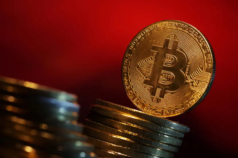 سکه طلایی بیت کوین (Bitcoin) روی دو دسته سکه در پس‌زمینه قرمز