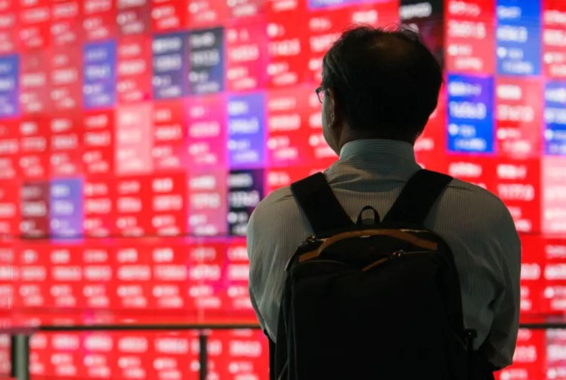 یک مرد آسیایی روبروی یک تابلو سراسر قرمز بورس 