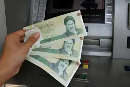 دستِ فردی که چند اسکناس ریال ایران را جلوی دستگاه خودپرداز نگه داشته است