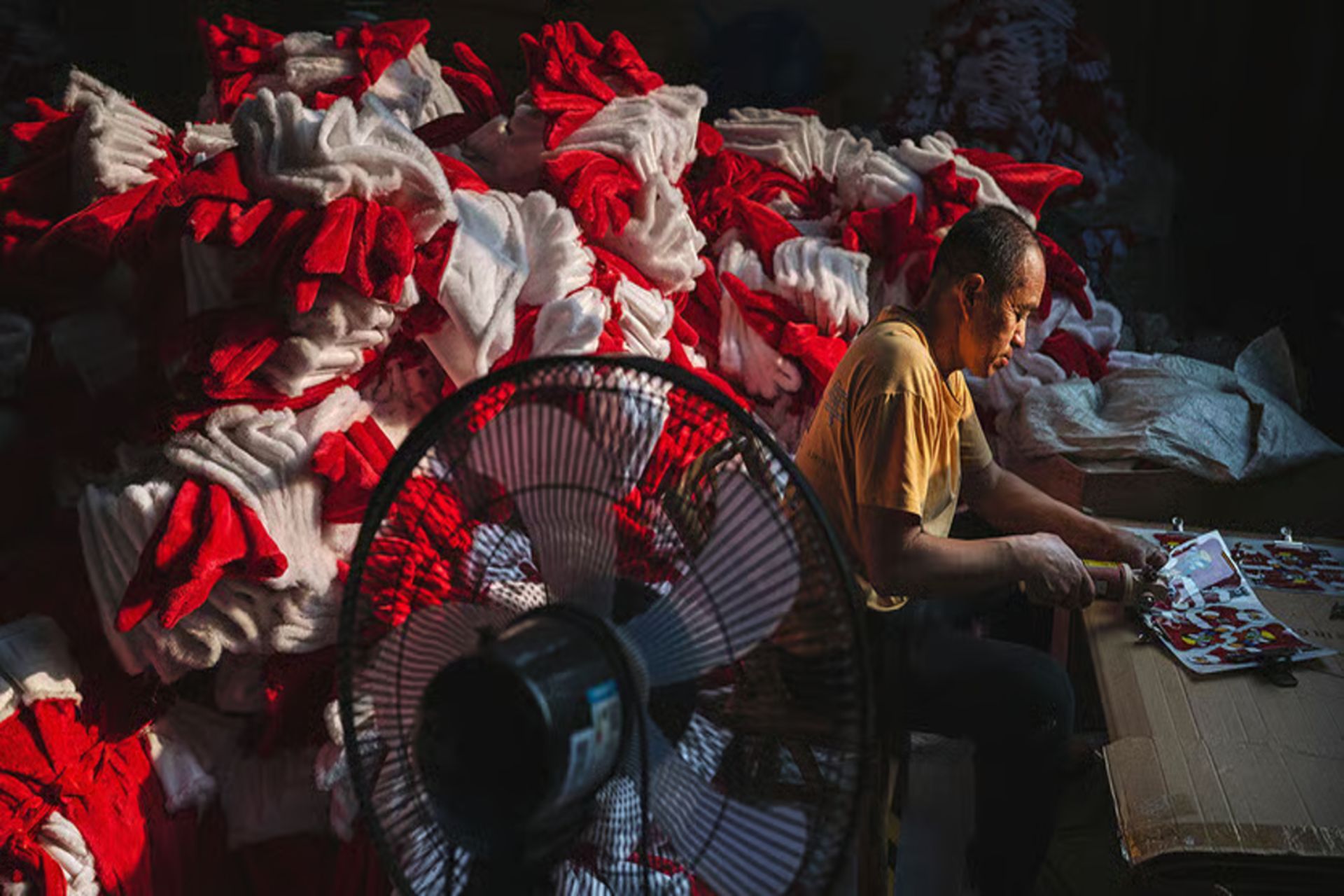 کارگری در کارگاه تولید تزئینات کریسمس در ییوو چین، در کنار انبوه لباس‌های بابانوئل