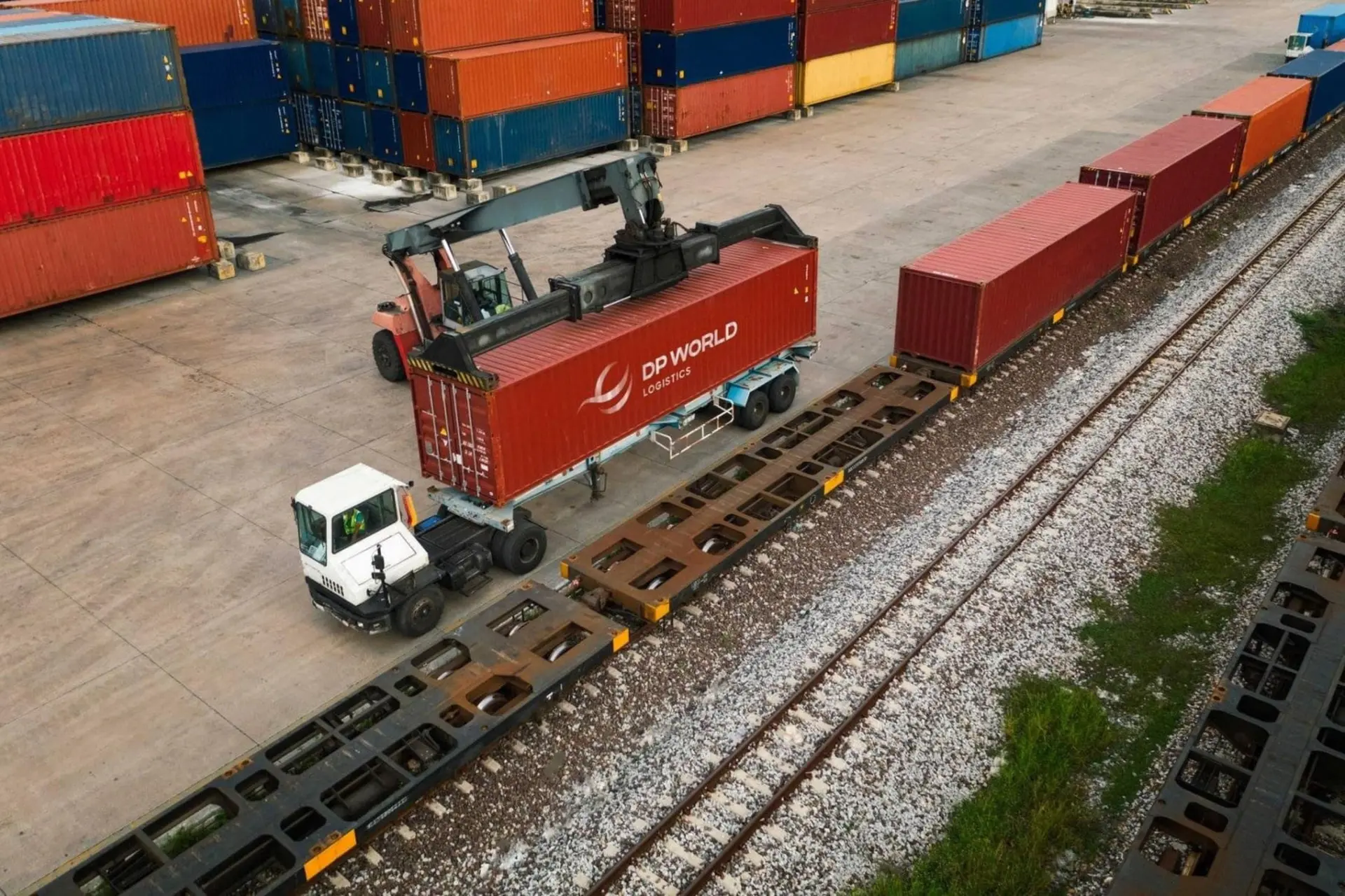 کانتینر قرمز برند دی‌پی ورلد (DP World) توسط جرثقیل روی واگن قطار باربری قرار می‌گیرد