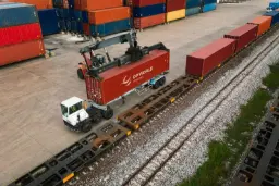 کانتینر قرمز برند دی‌پی ورلد (DP World) توسط جرثقیل روی واگن قطار باربری قرار می‌گیرد