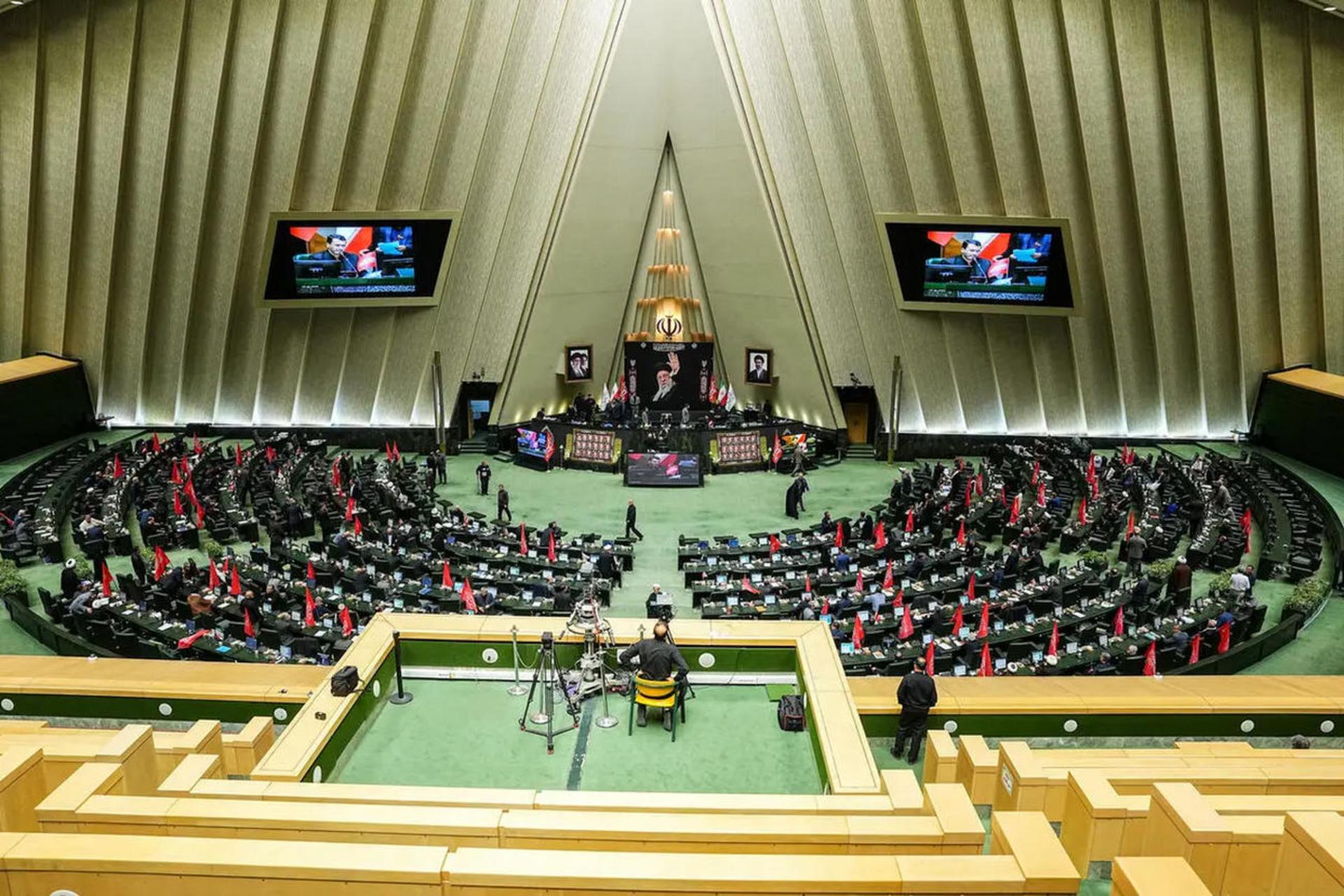 نمای باز از صحن علنی مجلس شورای اسلامی با نمایندگان مستقر در صندلی‌ها و نمایشگرهای بزرگ در پس‌زمینه.