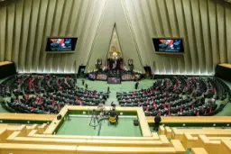 نمای باز از صحن علنی مجلس شورای اسلامی با نمایندگان مستقر در صندلی‌ها و نمایشگرهای بزرگ در پس‌زمینه.