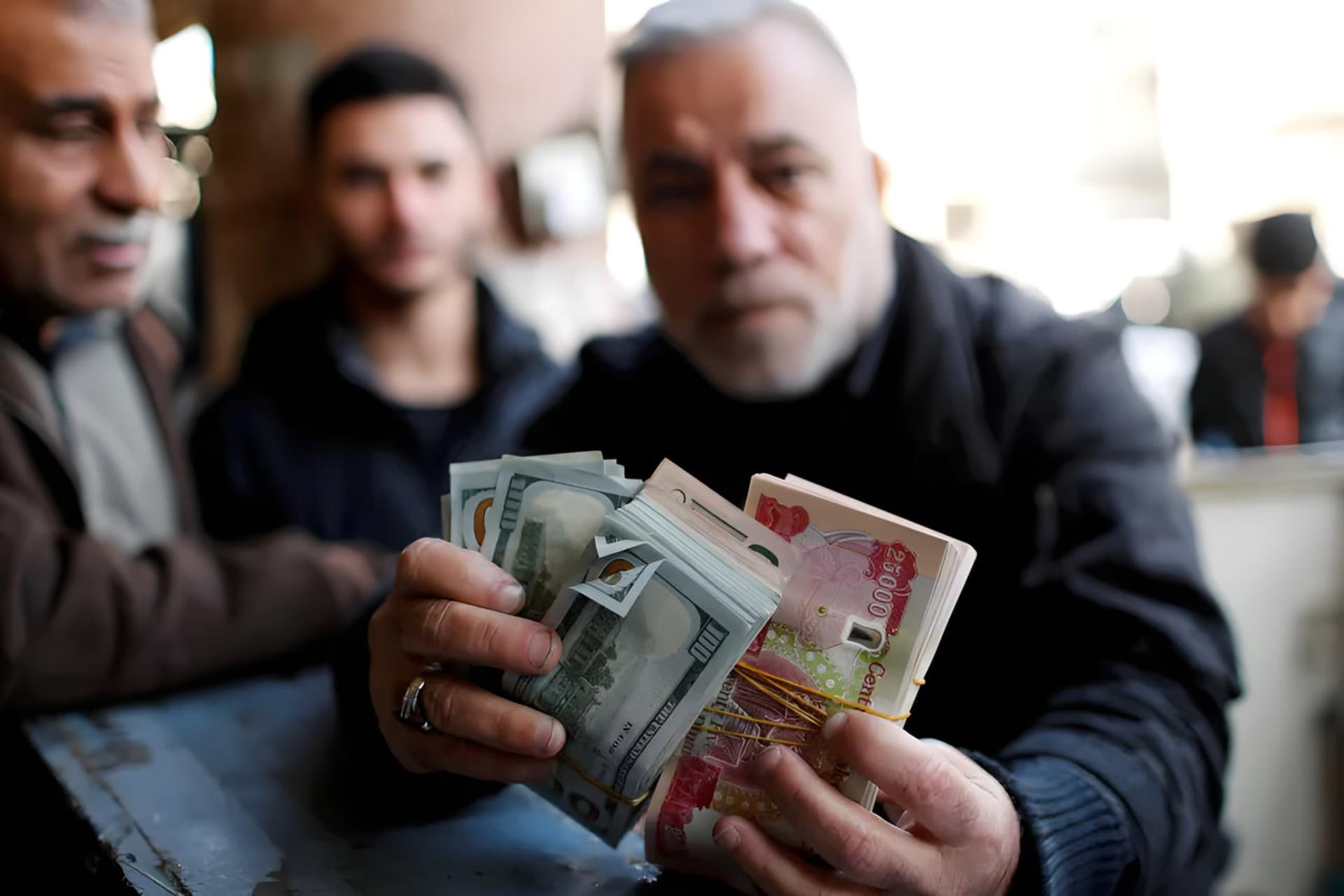 دست‌های مردی در بازار تبادل ارز بغداد با دسته‌های اسکناس دلار و دینار
