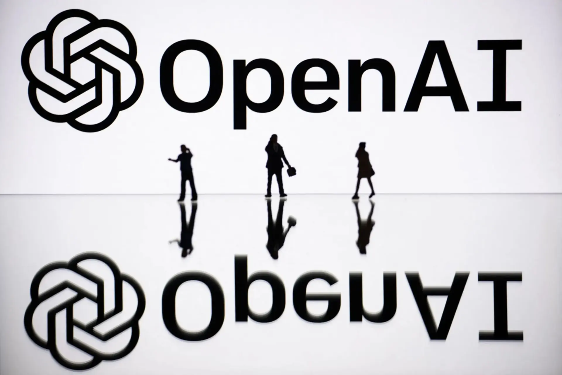 لوگوی شرکت OpenAI (OpenAI) در پس‌زمینه با سایه سه نفر در جلو