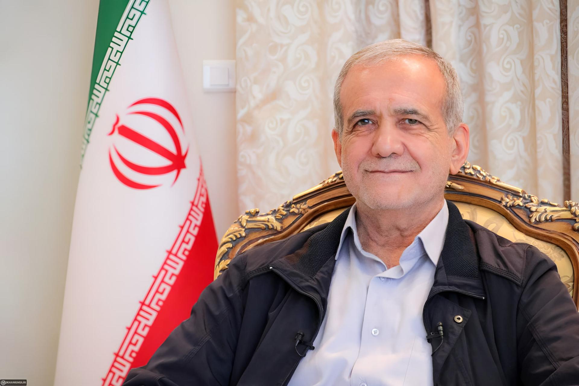 مسعود پزشکیان که در مقابل پرچم ایران نشسته است