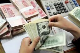 دست‌های فردی در حال شمارش اسکناس‌های دلار آمریکا در کنار بسته‌های پول یوآن