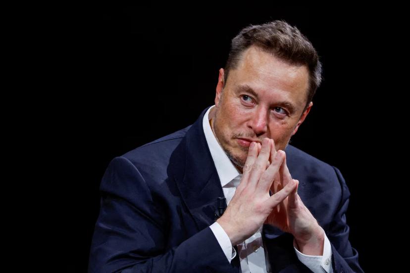 ایلان ماسک (Elon Musk) با دست‌های گره‌خورده در مقابل پس‌زمینه سیاه