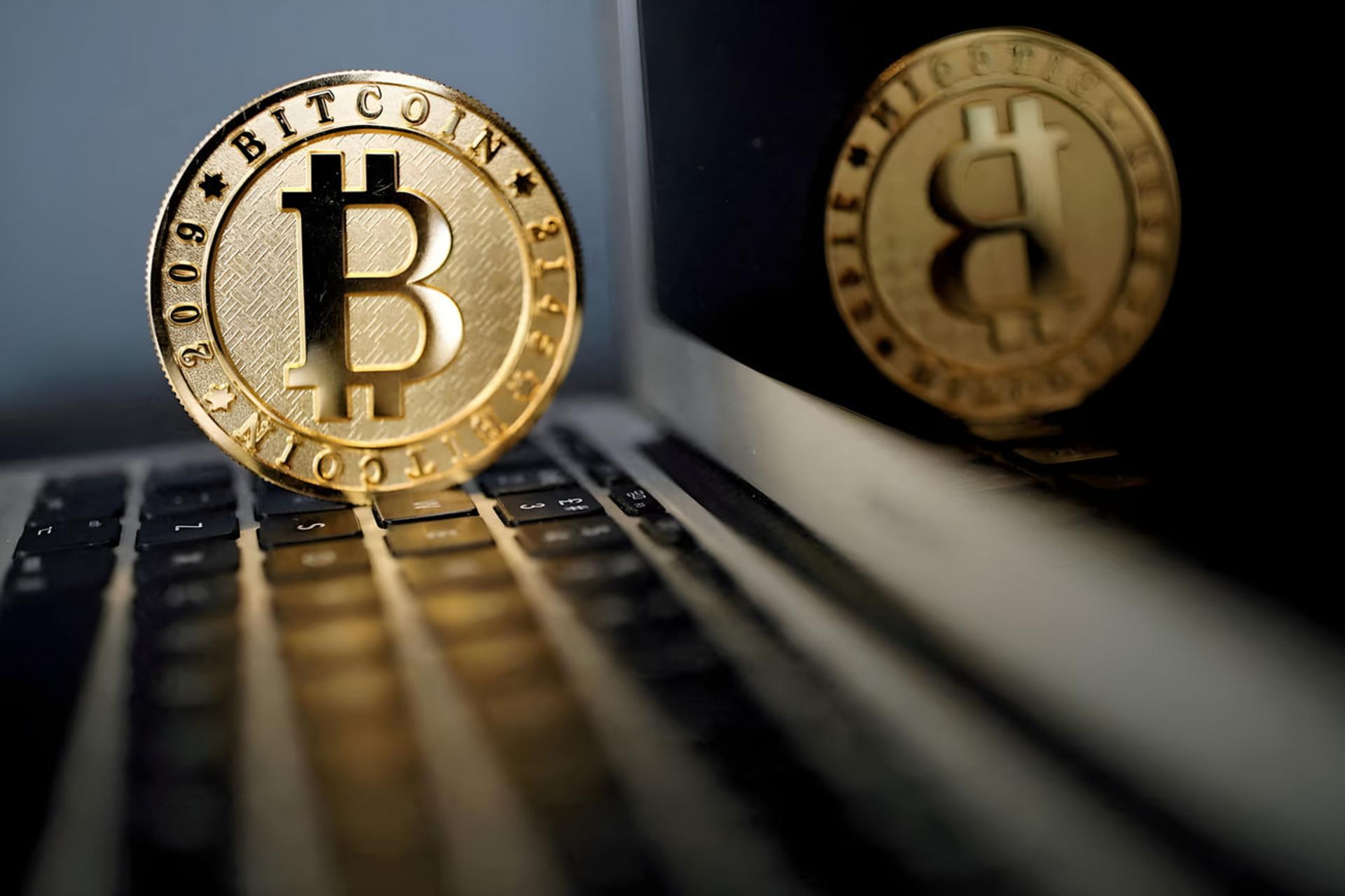 سکه طلایی بیت‌کوین (Bitcoin) روی صفحه‌کلید لپ‌تاپ در کنار نمایشگر