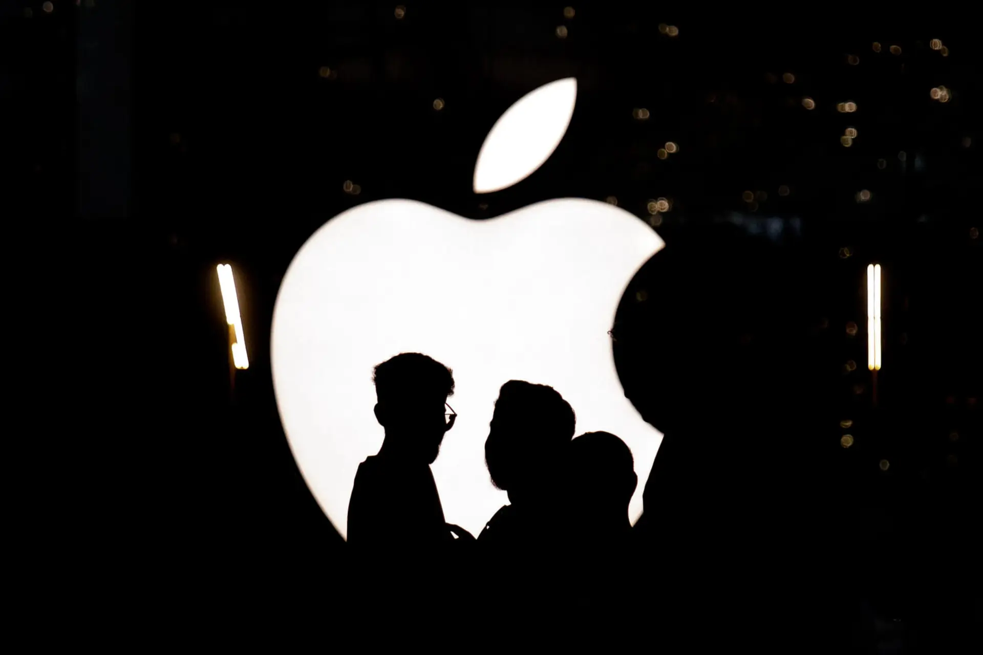 لوگوی اپل (Apple) در شب در مقابل سایه چند نفر