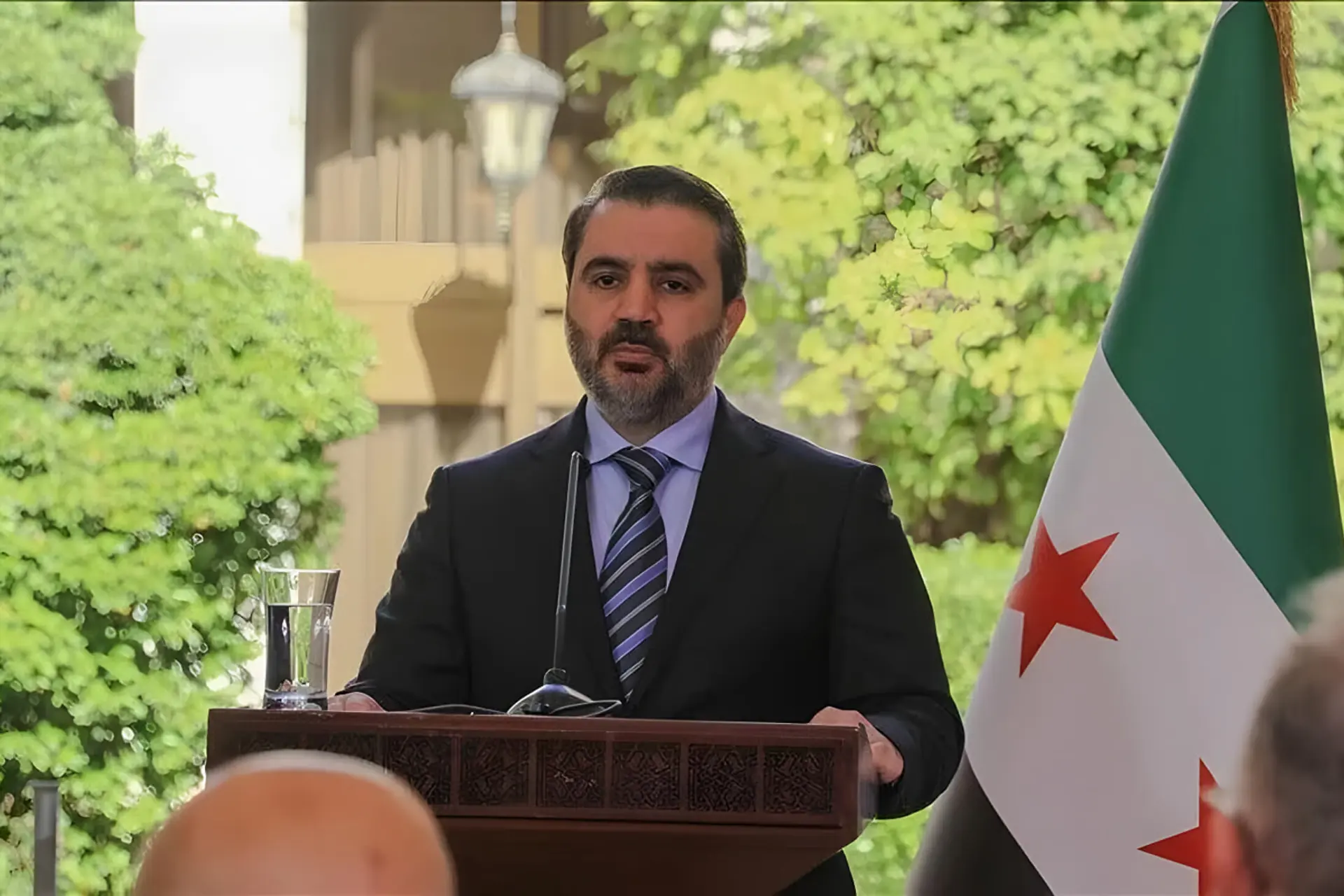 اسعد الشیبانی (As'ad al-Shaibani) در حال سخنرانی در کنار پرچم سوریه