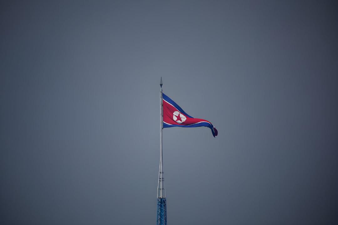 پرچم کره شمالی (North Korea) بر فراز یک دکل در آسمان صاف