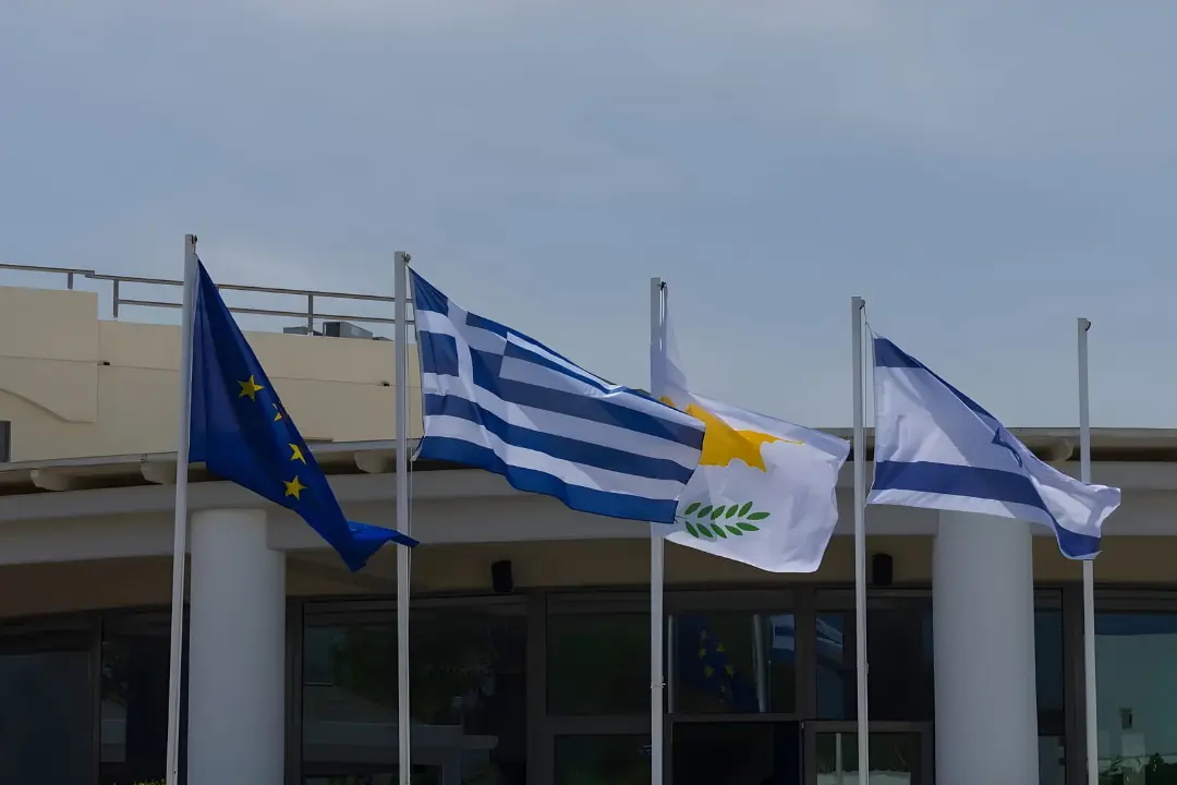 پرچم‌های اتحادیه اروپا (EU)، یونان (Greece) و قبرس (Cyprus) در مقابل یک ساختمان