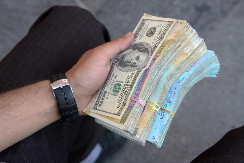 دسته اسکناس‌های دلار (USD) و ریال در دست یک فرد
