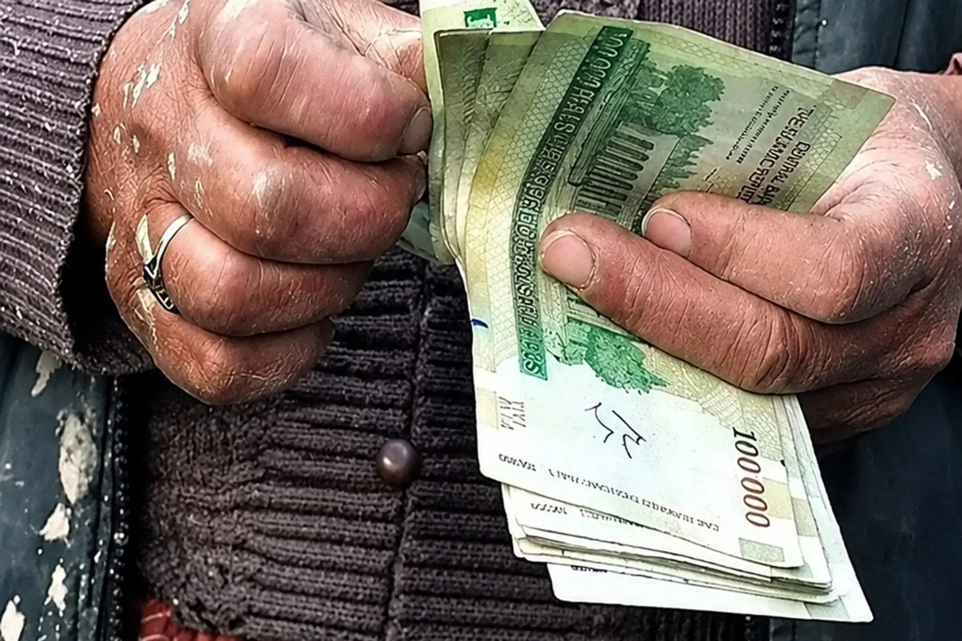 دست‌های کارگر با اسکناس‌های ۱۰۰ هزار تومانی ریال ایران