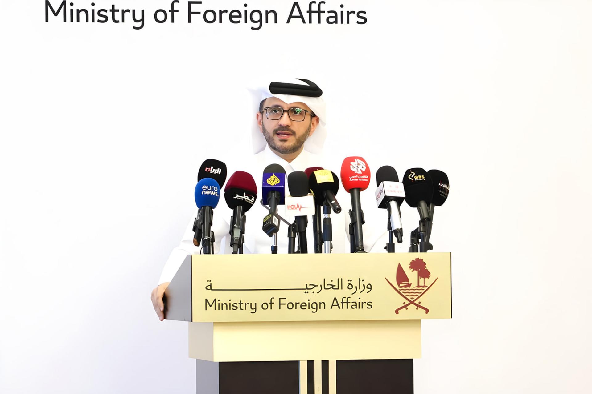 نماینده وزارت امور خارجه قطر (Ministry of Foreign Affairs) پشت میز کنفرانس با میکروفون‌های رسانه‌ای