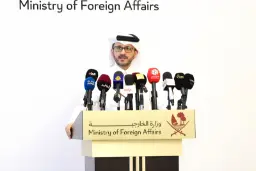 نماینده وزارت امور خارجه قطر (Ministry of Foreign Affairs) پشت میز کنفرانس با میکروفون‌های رسانه‌ای