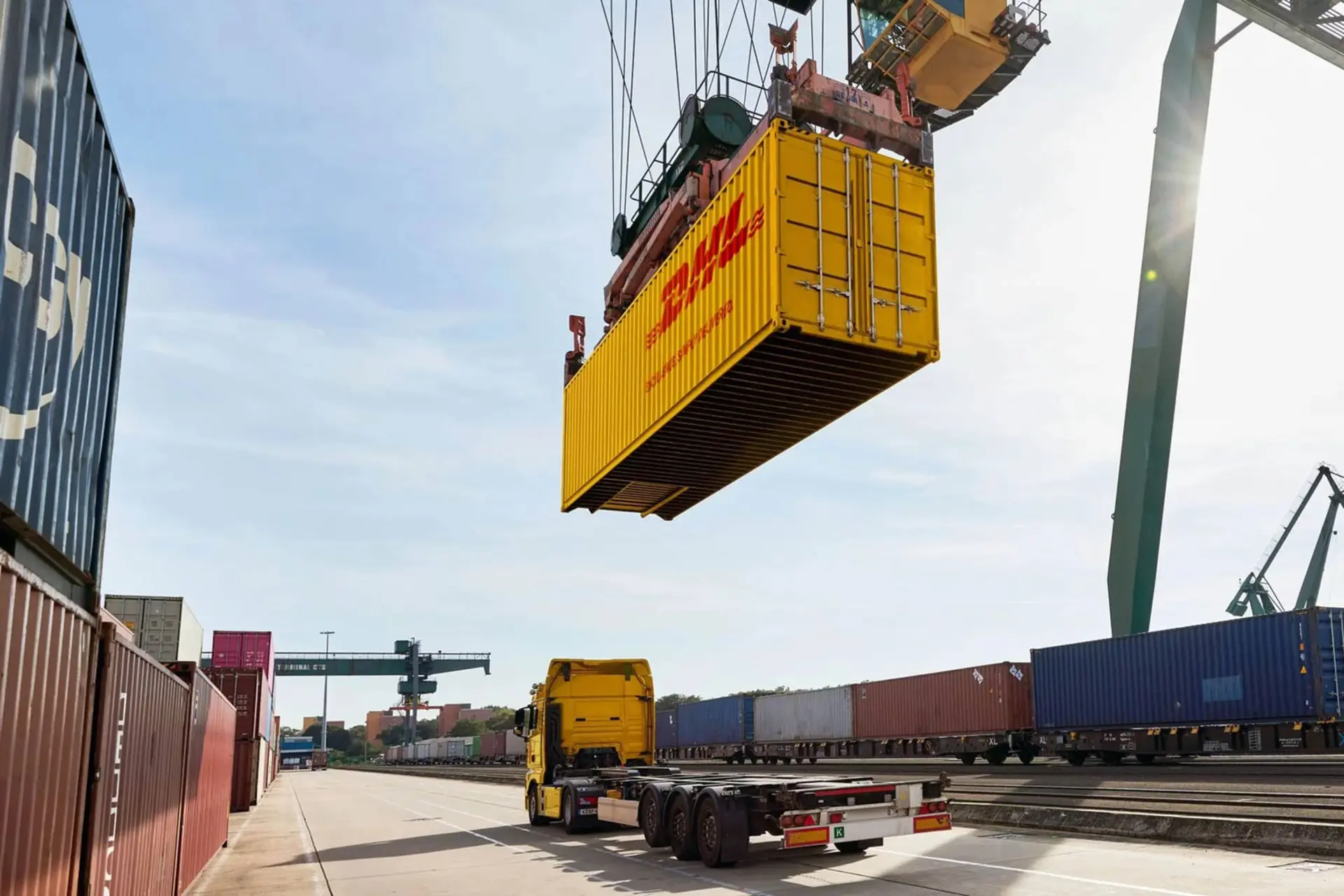 کانتینر زرد رنگ DHL توسط جرثقیل در مرکز لجستیک جابجا می‌شود
