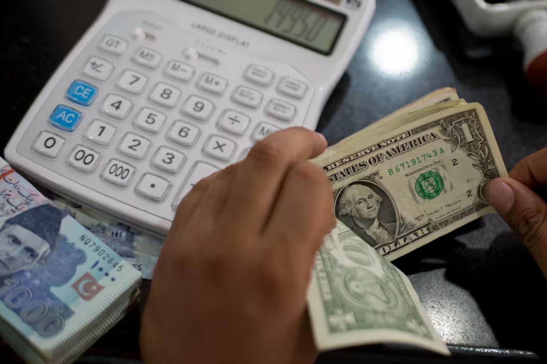 دست‌های فردی در حال شمارش اسکناس‌های یک دلاری (US Dollar) در کنار ماشین حساب