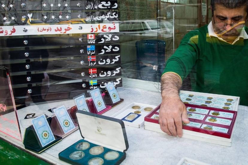 مردی در حال چیدمان سکه‌ها و اسکناس‌های قدیمی در ویترین یک مغازه تعویض ارز است.