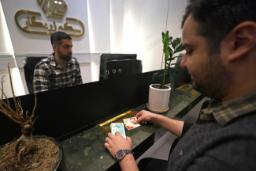 مردی در حال پرداخت اسکناس و کارت بانکی به کارمند صرافی پشت میز سیاه