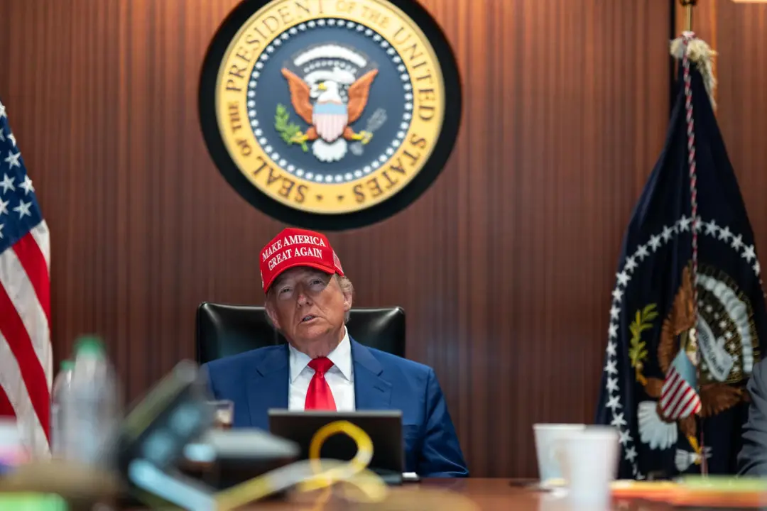 دونالد ترامپ با کلاه قرمز شعار Make America Great Again پشت نشان ریاست جمهوری آمریکا نشسته است.