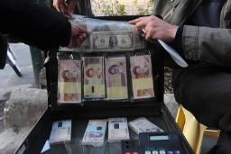 دست‌های افراد در حال جابه‌جایی بسته‌های پول نقد دلار (USD) و ریال ایران