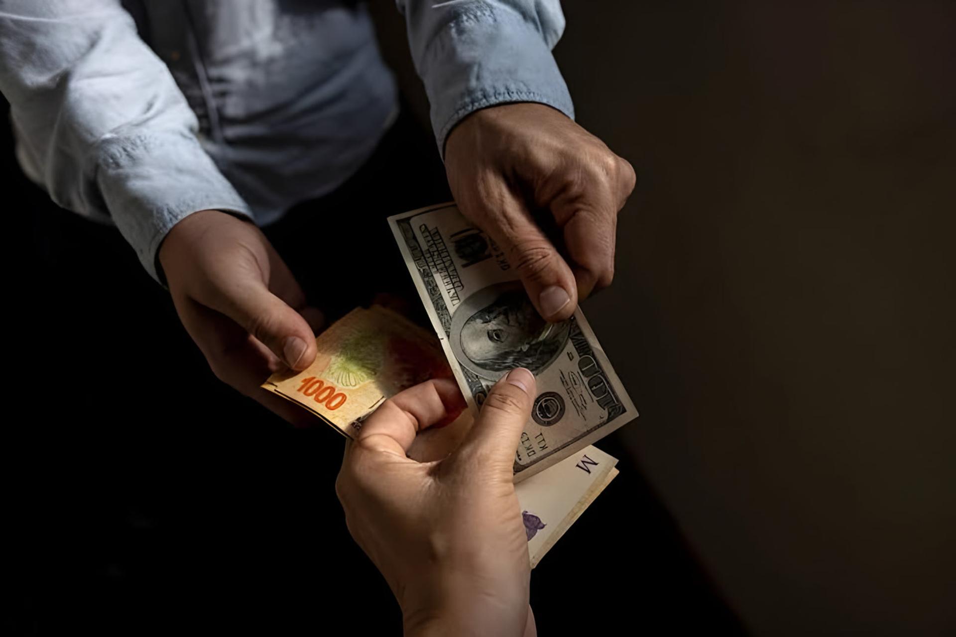 دست‌های دو نفر در حال رد و بدل کردن اسکناس‌های ۱۰۰ دلاری (USD) و پول محلی