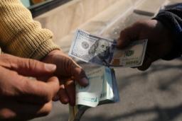نمای نزدیک از دست‌هایی که در حال رد و بدل کردن اسکناس‌های ۱۰۰ دلاری آمریکا با اسکناس‌های ریال ایران هستند.