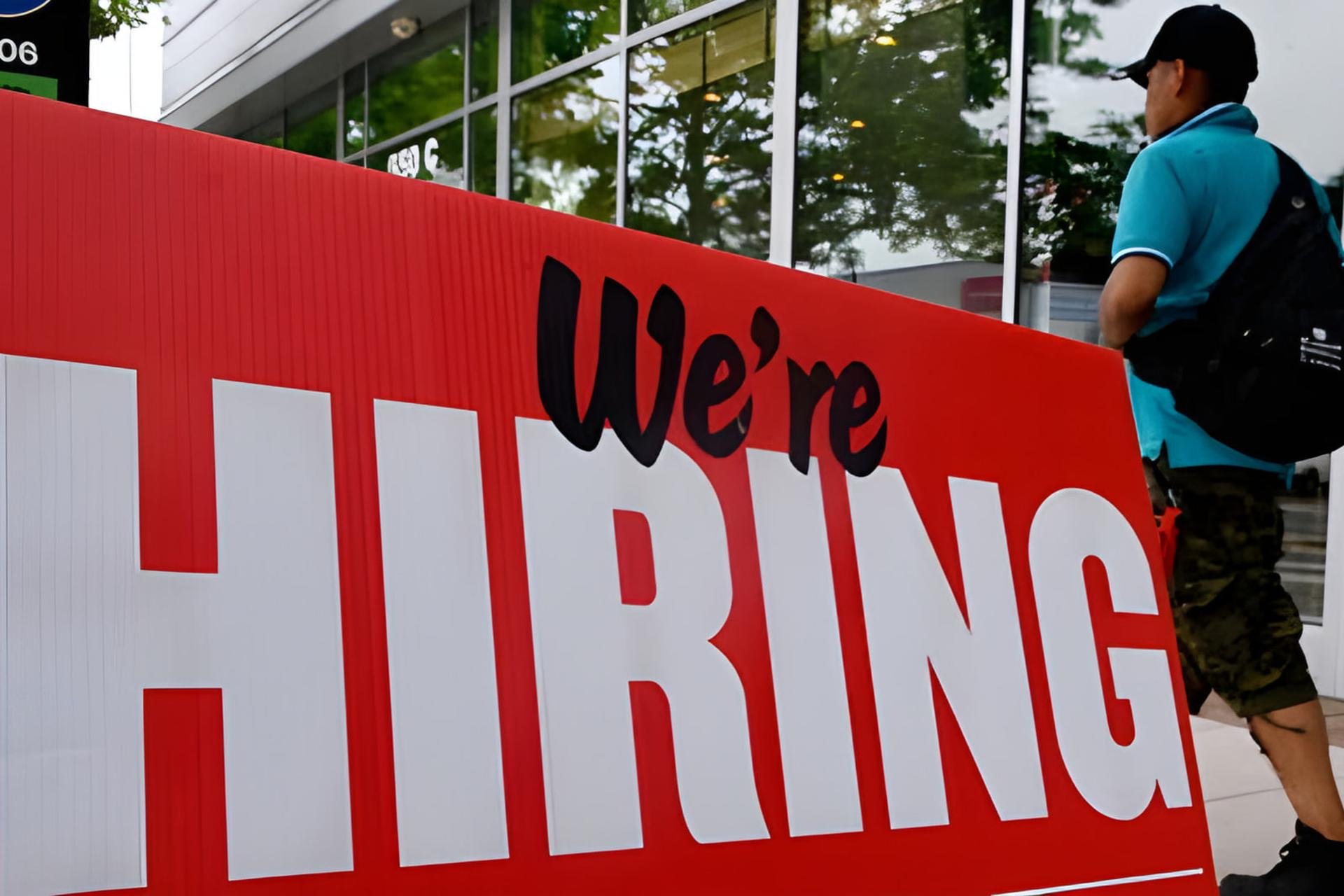 تابلوی قرمز رنگ با عبارت We're HIRING در فضای باز