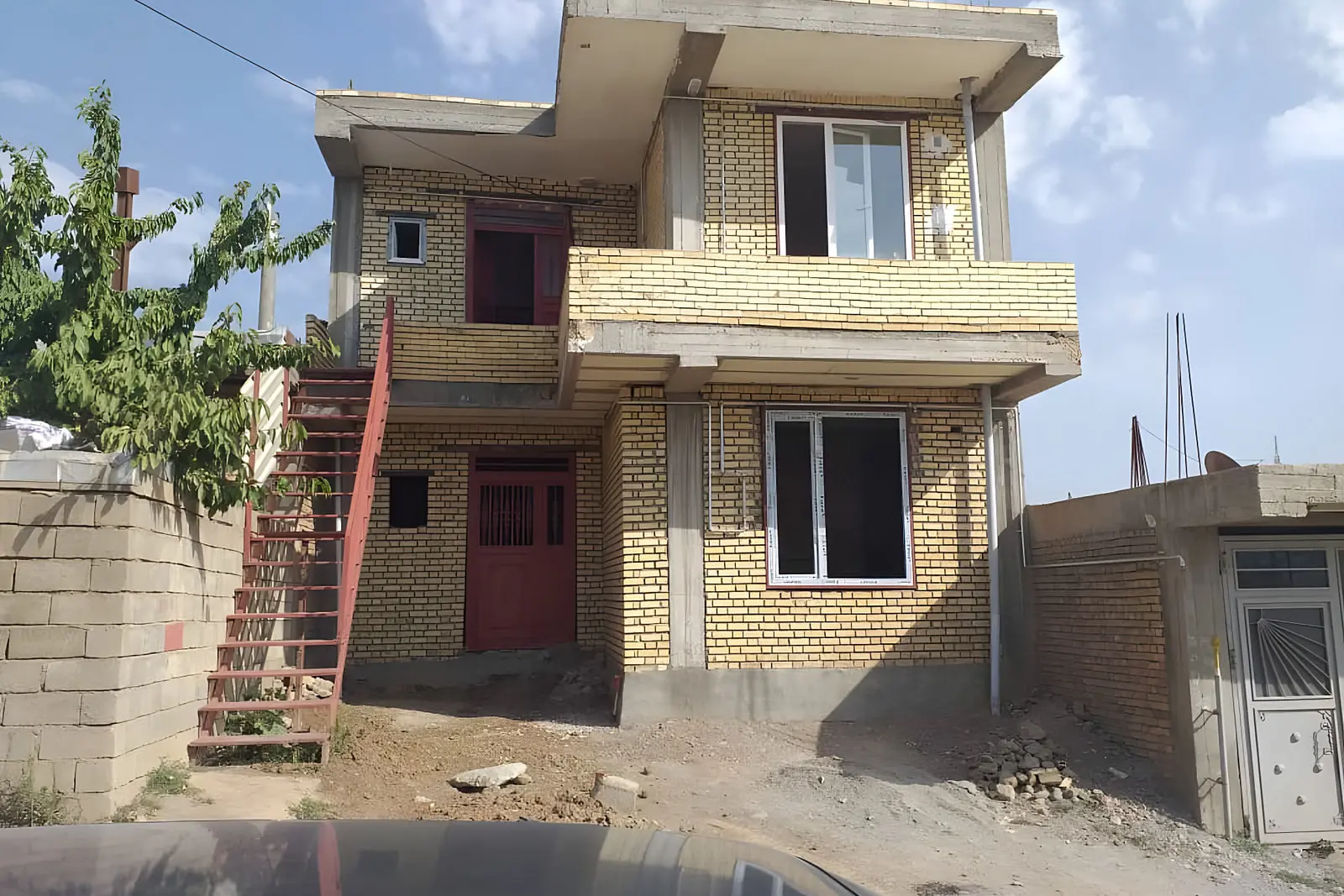 ساختمان دو طبقه با نمای آجری و بالکن در حال ساخت