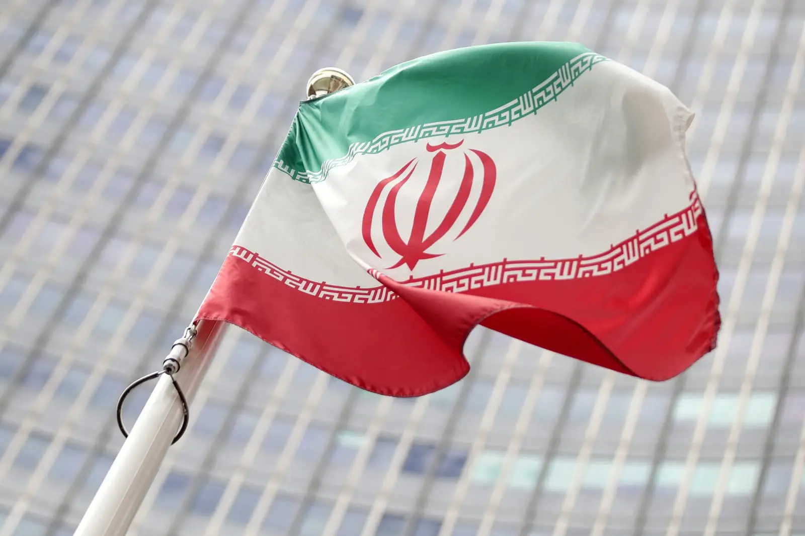 پرچم جمهوری اسلامی ایران (Flag of Iran) در مقابل نمای یک ساختمان بلند