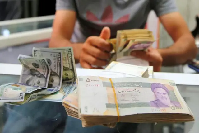 نمایی از دسته‌های اسکناس ریال ایران و اسکناس‌های صد دلاری آمریکا روی میز صرافی
