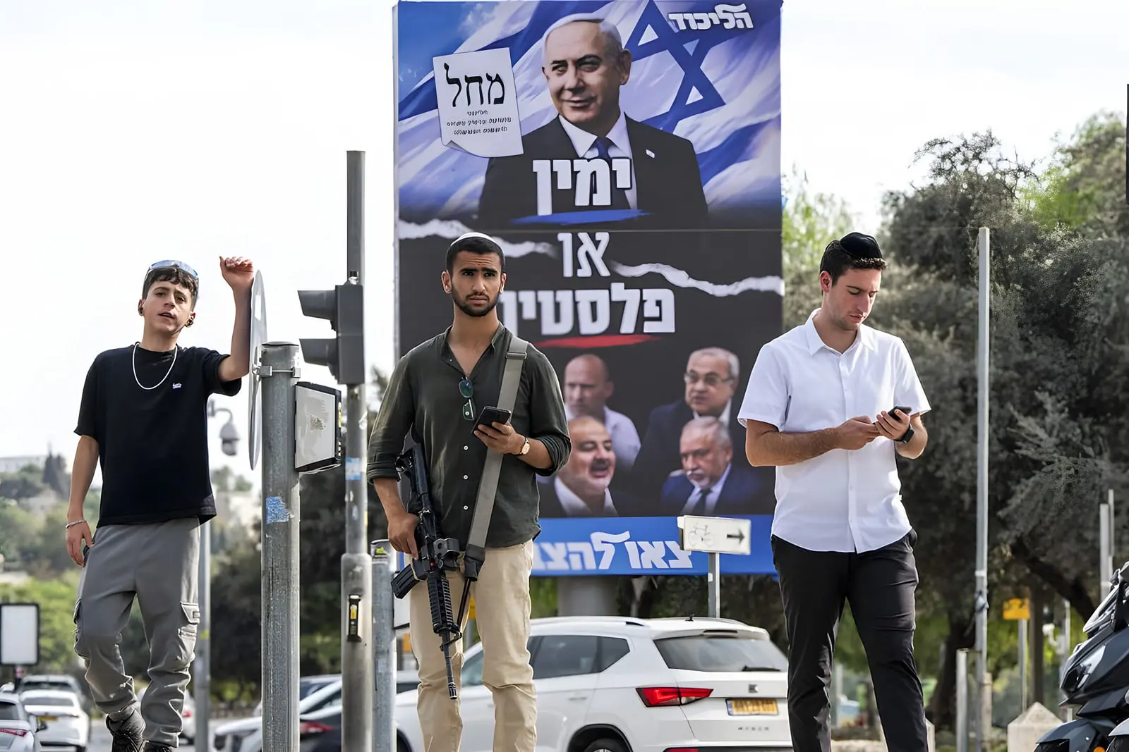 سرباز مسلح و جوانان در کنار بیلبورد تبلیغاتی بنیامین نتانیاه (Benjamin Netanyahu)