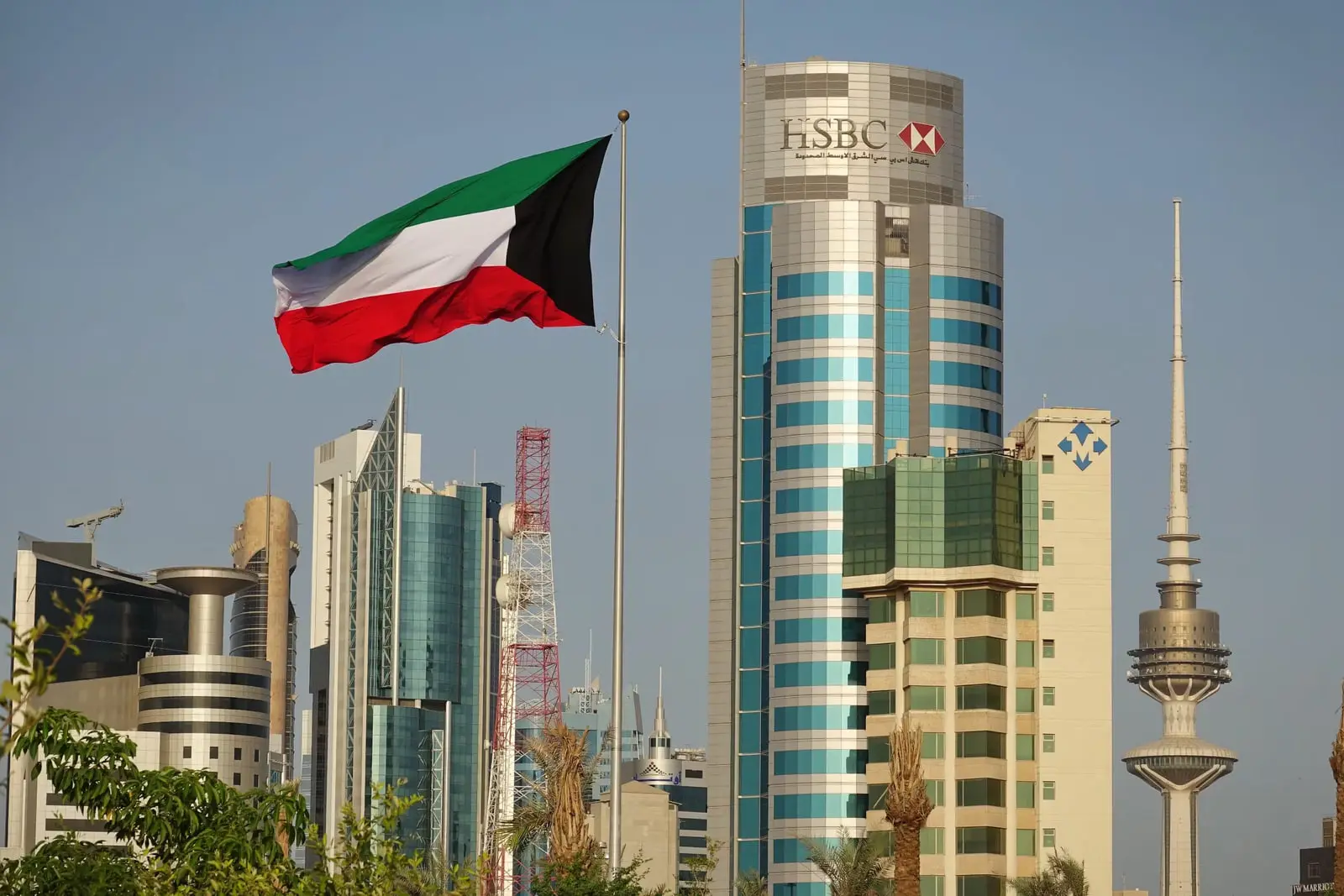 پرچم کویت (Kuwait Flag) در مقابل آسمان و ساختمان‌های بلند شهر