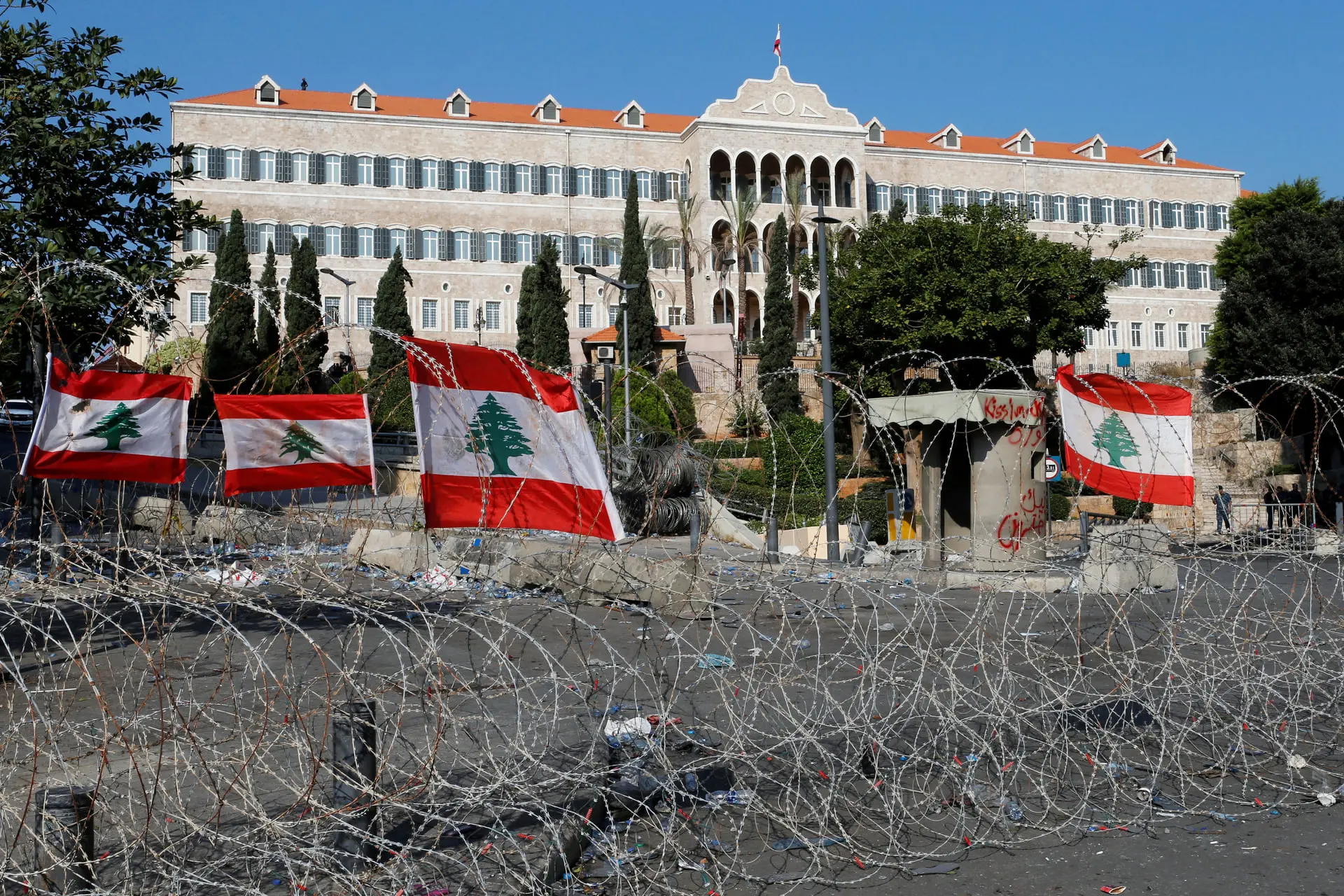 پرچم‌های لبنان (Lebanon) پشت حصار سیم خاردار در مقابل یک ساختمان بزرگ