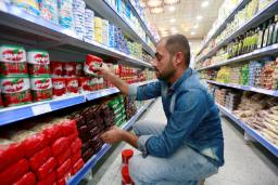 مردی در حال انتخاب قوطی‌های کنسرو از قفسه‌های فروشگاه