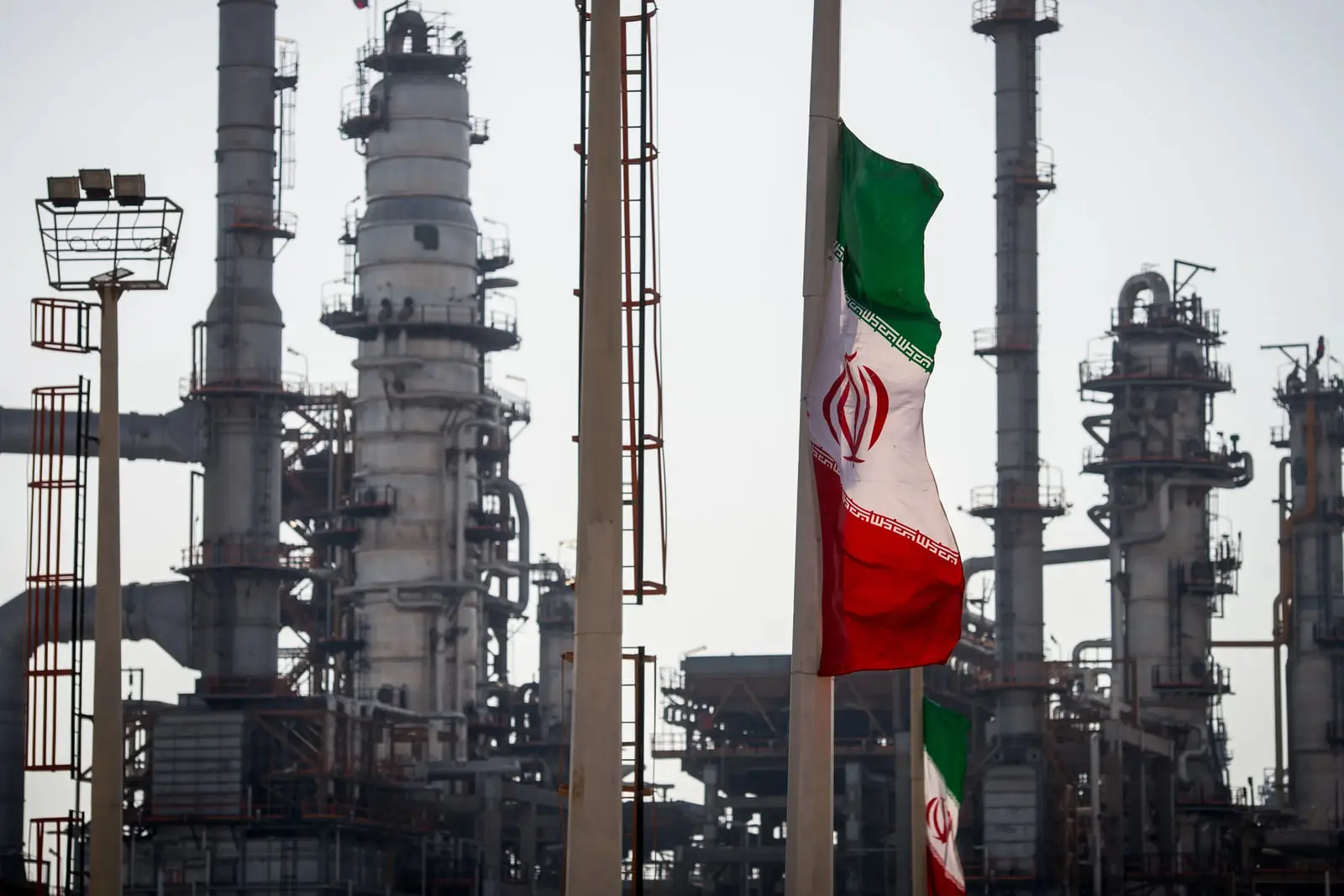 پرچم ایران (Flag of Iran) در مقابل برج‌های پالایشگاه نفت