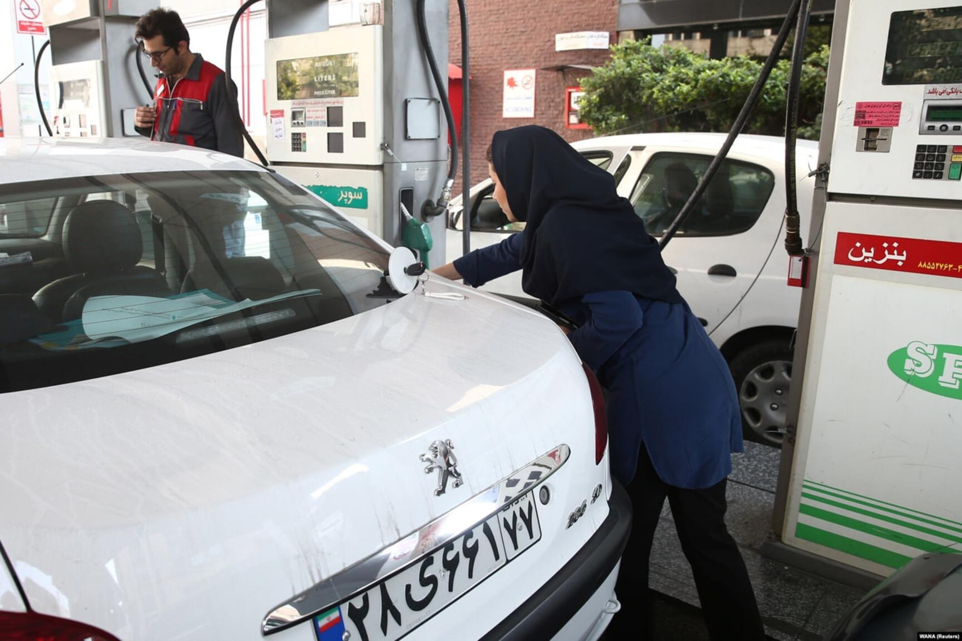 یک زن در حال سوخت‌گیری خودروی سفید در یک پمپ بنزین است.