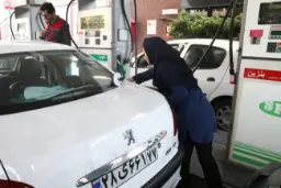 یک زن در حال سوخت‌گیری خودروی سفید در یک پمپ بنزین است.