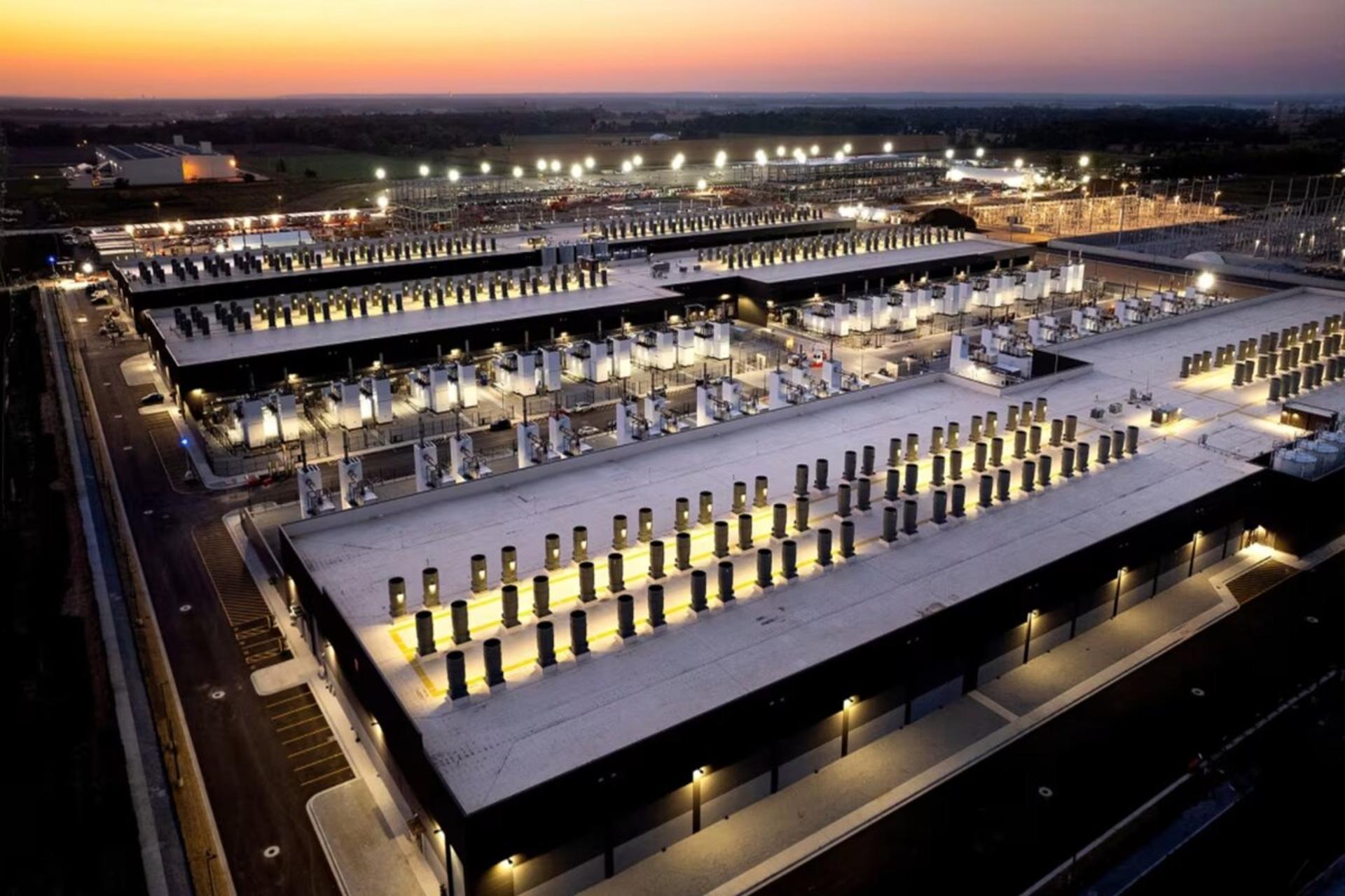 نمای هوایی از یک مرکز داده عظیم هوش مصنوعی با ردیف‌های طولانی سرورها و تجهیزات خنک‌کننده در زمان غروب