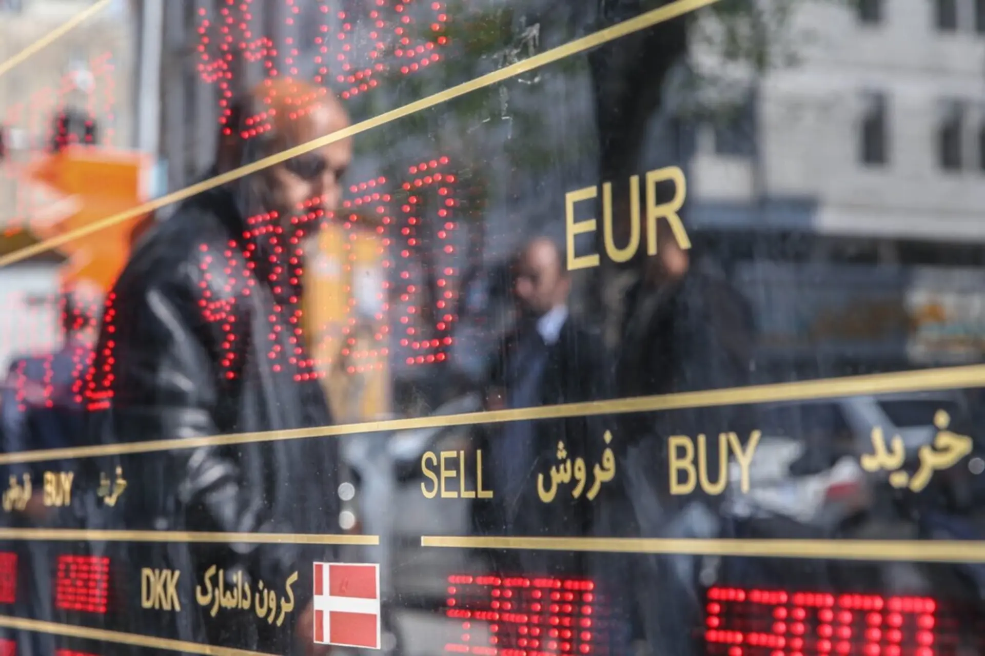 تابلو قیمت یک صرافی همراه با تصویری منعک شده یک معامله گر ارزی