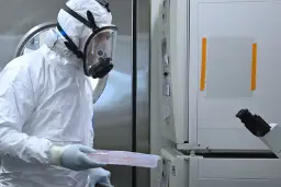 متخصص با لباس حفاظتی کامل (Hazmat Suit) در حال جابجایی نمونه‌ها در آزمایشگاه