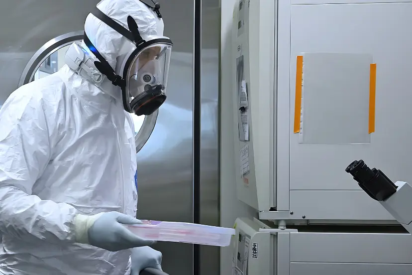 متخصص با لباس حفاظتی کامل (Hazmat Suit) در حال جابجایی نمونه‌ها در آزمایشگاه