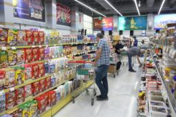 مردی در حال حرکت با چرخ‌دستی در راهروی فروشگاه مواد غذایی در کنار قفسه‌های پر از محصولات