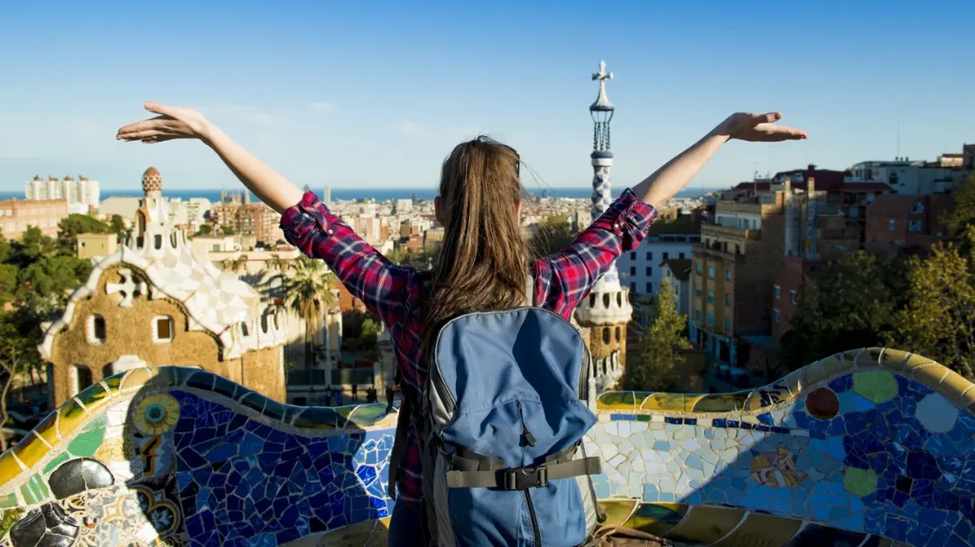 دختر مسافر با کوله‌پشتی در مقابل نمای شهر بارسلونا (Barcelona)